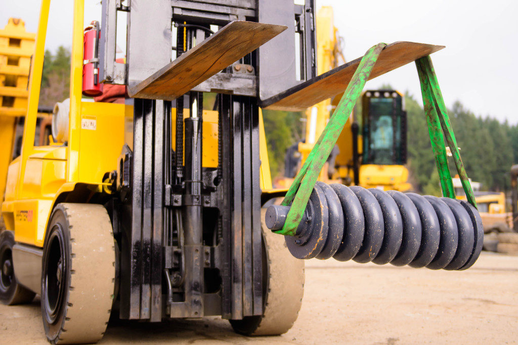 A forklift lifting a large coil spring. VI Equipment Ltd. offers a wide variety of used, rebuilt, and new excavator parts for Hitachi, John Deere, and Caterpillar excavators