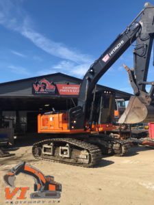 Large orange construction excavator parked in front of a building. The excavator has a long yellow arm and a black metal claw. This image is a relevant resource for finding excavator parts, spare parts, replacements, suppliers, and solutions.